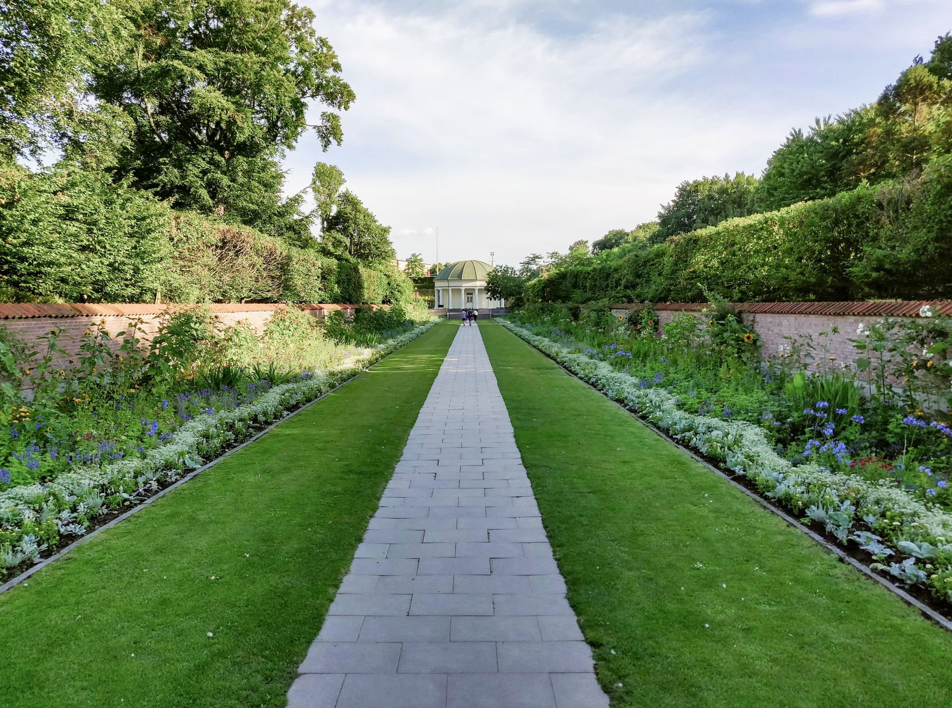 Garten mit langem Steinweg. Am Ende des Weges eine Kapelle mit grünem Dach.